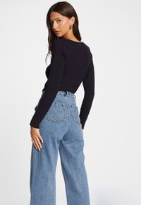 Marineblaue Langarmbluse mit rundem Halsausschnitt, kombiniert mit hellblauen hoch taillierten weit geschnittenen Jeans, die über eine Taschen hinten und eine strukturierte Oberfläche verfügen.