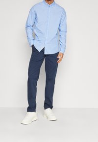 Lichtblauw gestreept overhemd met knopen, marineblauwe broek en witte sneakers. Heeft een standaard kraag en lange mouwen, met een ontspannen pasvorm.