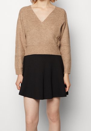 Knit, beige, V-neck cropped sweater with long sleeves above a black flared skirt. Features textured fabric and a fitted waist.