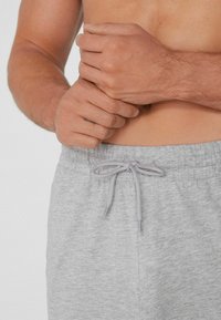 Gray drawstring shorts made of soft fabric, featuring a gathered waistband and matching drawcord detail. Close-up of hands on waist.