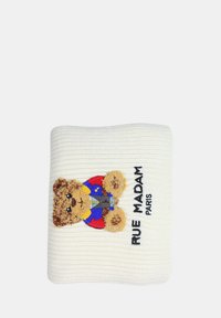 Hvid strikket pude med en broderet bjørn iført et farverigt outfit og holder en mikrofon, med teksten "RUE MADAM PARIS" nedenfor.