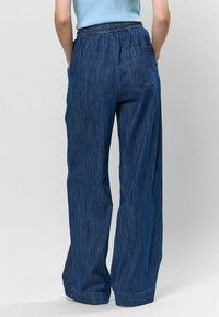 Pantaloni din denim largi, de culoare albastru închis, cu un brâu elastic, o pungă la spate și o textură ușoară. Marginea are un finisaj simplu și curat.
