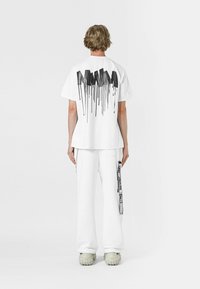 Camiseta blanca con un diseño de goteo de pintura negra en la parte posterior, combinada con pantalones blancos que tienen una franja gráfica negra a lo largo del costado.