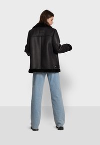 Black leather jacket with fur collar, boxy fit, and wide sleeves. Hem features a soft fur trim; back has a smooth texture and minimal detailing.