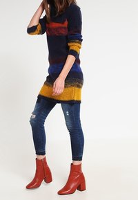 Pull en tricot à rayures multicolores (bleu marine, rouge, jaune) associé à un jean skinny bleu déchiré et des bottines rouges à talons carrés.