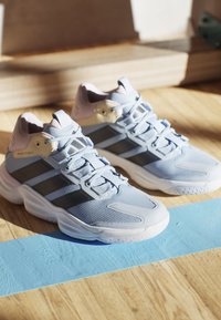 Scarpe da corsa azzurro chiaro con tomaia in rete, accenti scuri e collare imbottito. Presentano una suola testurizzata e un sistema di allacciatura prominente.
