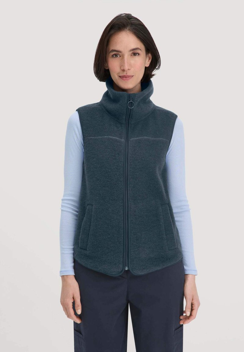 Dunkelgraue Fleeceweste mit hohem Kragen, Frontreißverschluss und zwei Seitentaschen, getragen über einem hellblauen Langarmshirt. Glatte Textur.