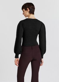Maglione nero a maglia con maniche a sbuffo strutturate, vita adatta e scollo a coste, abbinato a pantaloni bordò sartoriali con tasche posteriori.