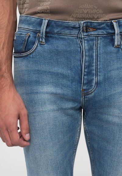 Világoskék farmernadrág, slim fit szabással, narancssárga varrásokkal, elülső zsebbel és gombos záródással. Egyszerű és klasszikus dizájn.