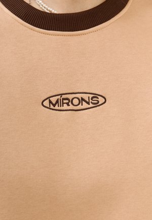 T-shirt di cotone color tela con colletto a coste marrone, caratterizzata da un logo ricamato nero che riporta la scritta "MIRÓNS" in forma ovale al centro.