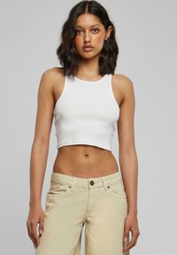 Hvit avkortet tank topp med rund halslinning, laget av myk bomull; kombinert med høyt liv beige vide jeans, som har frontlommer.