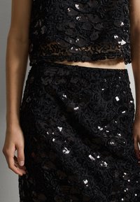 Zwart twee-delig outfit met een cropped, doorzichtige top en een hoge taille rok, versierd met ingewikkelde floral borduursels en pailletten.