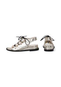 Metalické stříbrné sandály se slingback designem, zdobené černými šňůrkami a kulatými ozdobami na nártu. Plná černá podrážka.