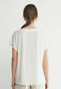 Hvid, løs siddende kortærmet top med en bred halsudskæring. Glat tekstur med et afslappet fald, der har et minimalistisk design.