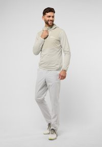 Lichtgrijze sportieve hoodie met een contrasterend lichtbeige borstpaneel, gecombineerd met lichtgrijze broek en neutraalgekleurde hardloopschoenen.