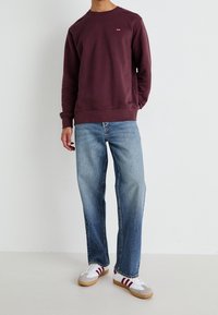 Bordeaux crewneck tröja med ribbad mudd, bleka blå raka jeans och vita sneakers med röda ränder. Minimalistisk avslappnad outfit.