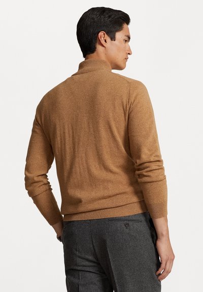 Brun stickad tröja med hög krage och ribbade ärmar, bärs med grå byxor. Den mjuka texturen och den figurnära designen framhäver den avslappnade stilen.