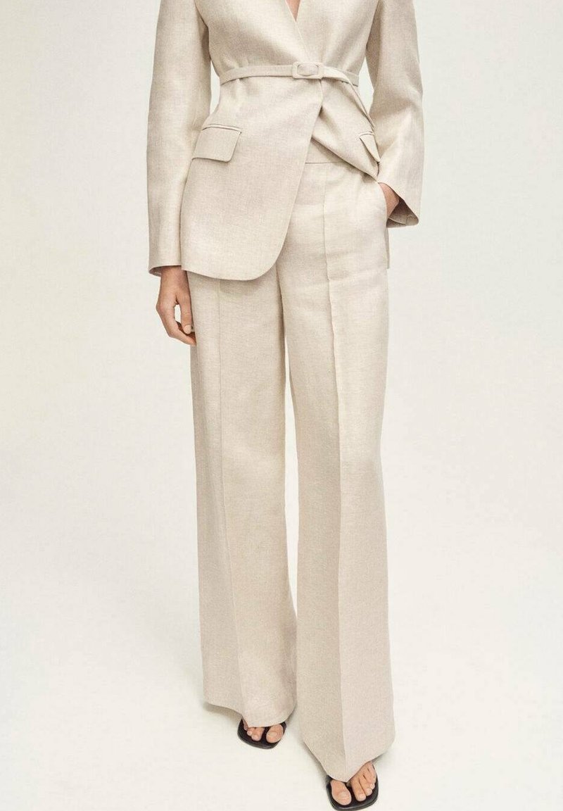 Costume en lin beige avec un blazer structuré ceinturé à la taille et un pantalon à jambes larges. Texture lisse avec un design minimaliste sans motifs.