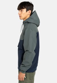Giacca con cappuccio caratterizzata da un design bicolore in verde e blu navy, con tasca frontale, cordoncino regolabile e polsini elasticizzati.