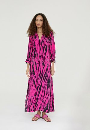 Largo vestido rosa con rayas negras, escote en V y mangas enrolladas. Diseño cortado con aberturas laterales, complementado con sandalias planas rosas.