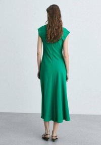 Grön klänning med kapprogade ärmar, åtsittande bodice och utsvängd kjol. Slät tyg, knälång och med en subtil detalj av bakseam.