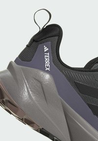 Černá a šedá sportovní bota s texturovaným svrškem, šedou gumovou podrážkou se zřetelným vzorem a smyčkou pro snadné nazouvání.
