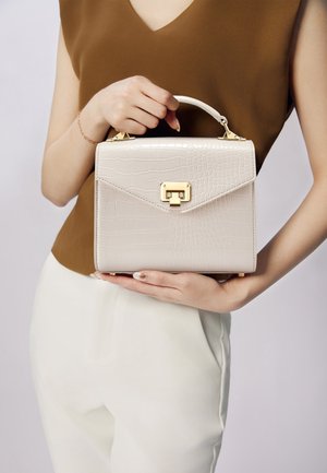 Krokodillenpatroon, lichtbeige handtas met een bovenhandvat en gouden hardware, voorzien van een klepsluiting en een slanke rechthoekige vorm.