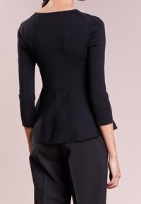 Černý peplum top se třičtvrtinovými rukávy, strukturovanou tkaninou, kulatým výstřihem a upnutým pasem, v kombinaci s přesně střiženými černými kalhotami.