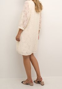 Blonde kjole i creme med trekvart gennemsigtige ærmer, struktureret blomster mønster og en løs pasform. Kombineret med tofarvede blok-hæle sko.