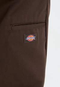Pantalon de travail en tissu brun avec un petit patch tissé "Dickies". Comprend une poche latérale avec une finition soignée et solide.