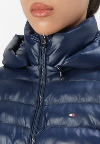 Navy puffer jacket with a zippered front and a high collar, featuring quilted sections and a small logo on the chest. Smooth texture.