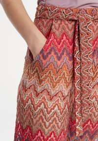 Jupe maxi avec un motif en zigzag dans des teintes de rouge, orange et bleu. Fabriquée en tissu texturé, avec une ceinture à nouer et une poche latérale.