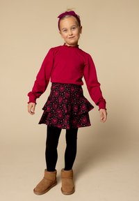 Rode langemouwen top met rimpelrand, zwarte rok met roze hartpatronen, zwarte legging en bruine enkelboots. Hoofdband past bij de top.