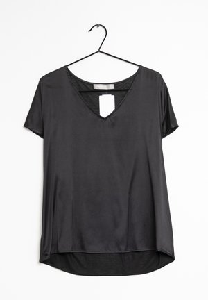Blouse noire à manches courtes avec col en V et légère brillance, suspendue à un cintre noir sur un fond blanc, avec une étiquette de prix visible à l'intérieur.