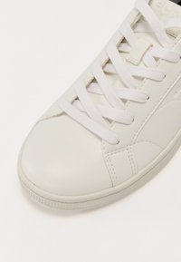 Sneaker bianco in pelle con punta rotonda, lacci bianchi piatti e pannello laterale testurizzato. Finitura liscia con sottili dettagli di cucitura.