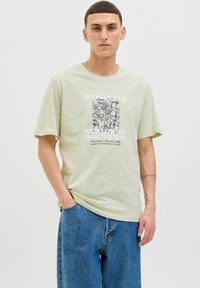 Lysegrøn bomulds T-shirt med korte ærmer, prydet med et grafisk print i marineblå samt hvid tekst; parret med løst sittende blå denimjeans.