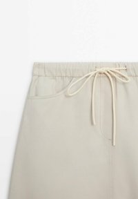 Pantalon beige clair à taille élastique avec poches avant et fermeture par cordon noué au centre devant.
