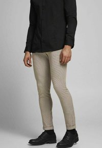 Beige rutiga byxor med slim fit, tillsammans med en svart långärmad skjorta och svarta läderskor.