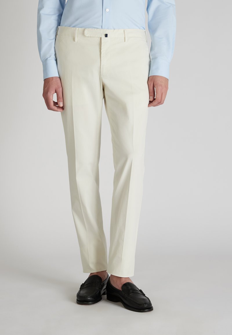 Pantaloni beige chiaro realizzati in tessuto morbido, con design a gamba dritta e sottili pieghe, abbinati a mocassini neri e una camicia azzurro chiaro.