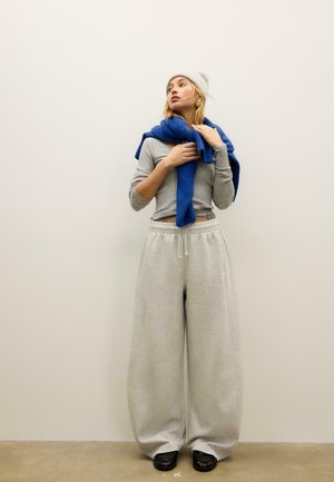 Volnena kapa, modra ruta, sivi rebrasti dolg rokav pulover, široke sive trenirka hlače in črni čevlji. Preprost dizajn z ohlapno prileganjem in mehko teksturo.