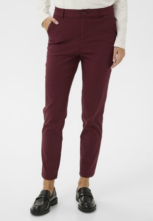 Burgundyanische Stretch-Baumwollhose mit schmaler Passform, Fronttaschen und Knopfverschluss. Kombiniert mit schwarzen Slippern.