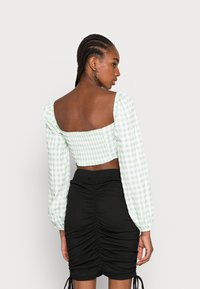 Top crop xadrez verde e branco com mangas bufantes e costas quadradas, combinado com uma saia mini preta com franzidos.