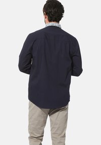 Navyblaues Langarmhemd mit gemustertem Kragen. Der Stoff wirkt glatt und leicht und hat einen leicht abgerundeten Saum.