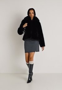 Casaco de pele sintética preto, curto, com um colarinho largo; saia mini de pele cinza; botas pretas até ao joelho com acabamento texturizado; meias brancas.