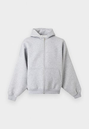 Ανοιχτό γκρι φούτερ με φερμουάρ, μπροστινές τσέπες και διακριτικές διακοσμήσεις με καρφιά στη κουκούλα και στα μανίκια, εμφανίζεται σε απλό φόντο.