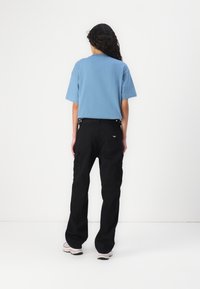 Blue cotton t-shirt with short sleeves paired with black cargo pants featuring pockets, worn with light-colored shoes, viewed from the back.