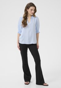 Blusa azul clara con escote en V y mangas cortas abullonadas, combinada con pantalones acampanados negros. La blusa presenta un escote con volantes.