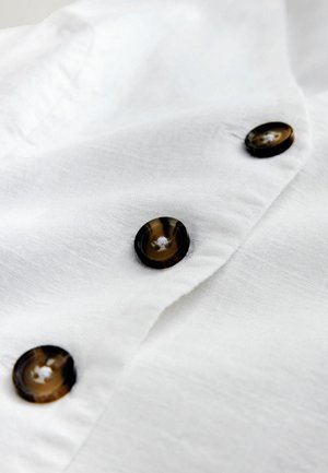 Biely textil s tromi tmavohnedými, okrúhlymi gombíkmi prišitými v zvislom rade.