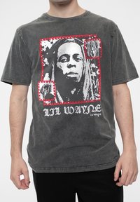 Cotton graphic t-shirt in dark gray featuring a central black-and-white portrait with red accents and the text "Lil Wayne" in white.