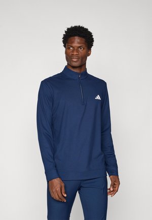 Pull-over à manches longues navy en tissu lisse avec un demi-zip et un col. Présente un petit logo blanc sur la poitrine gauche.